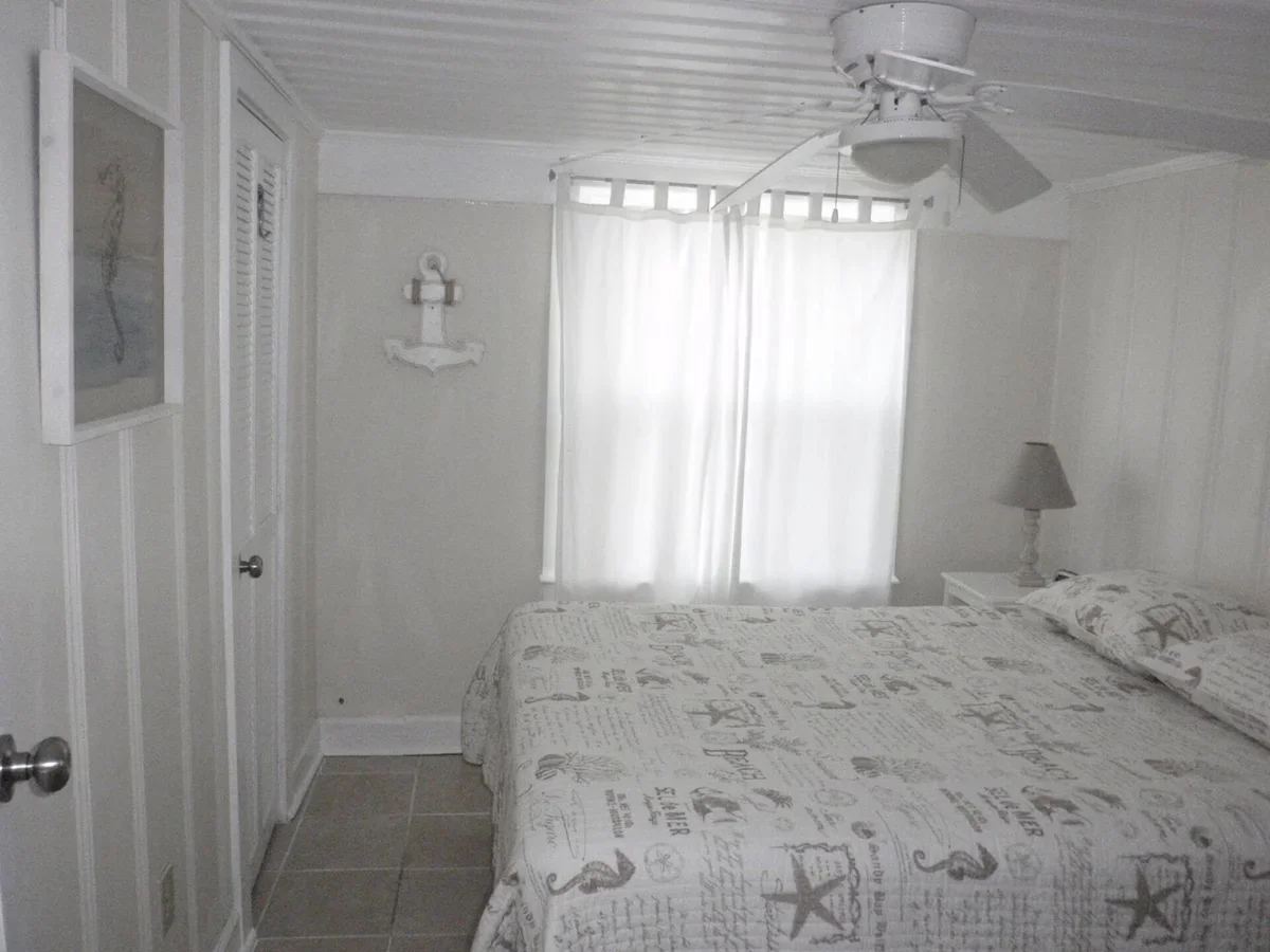 Bedroom with a bed, white curtains, ceiling fan and closet door