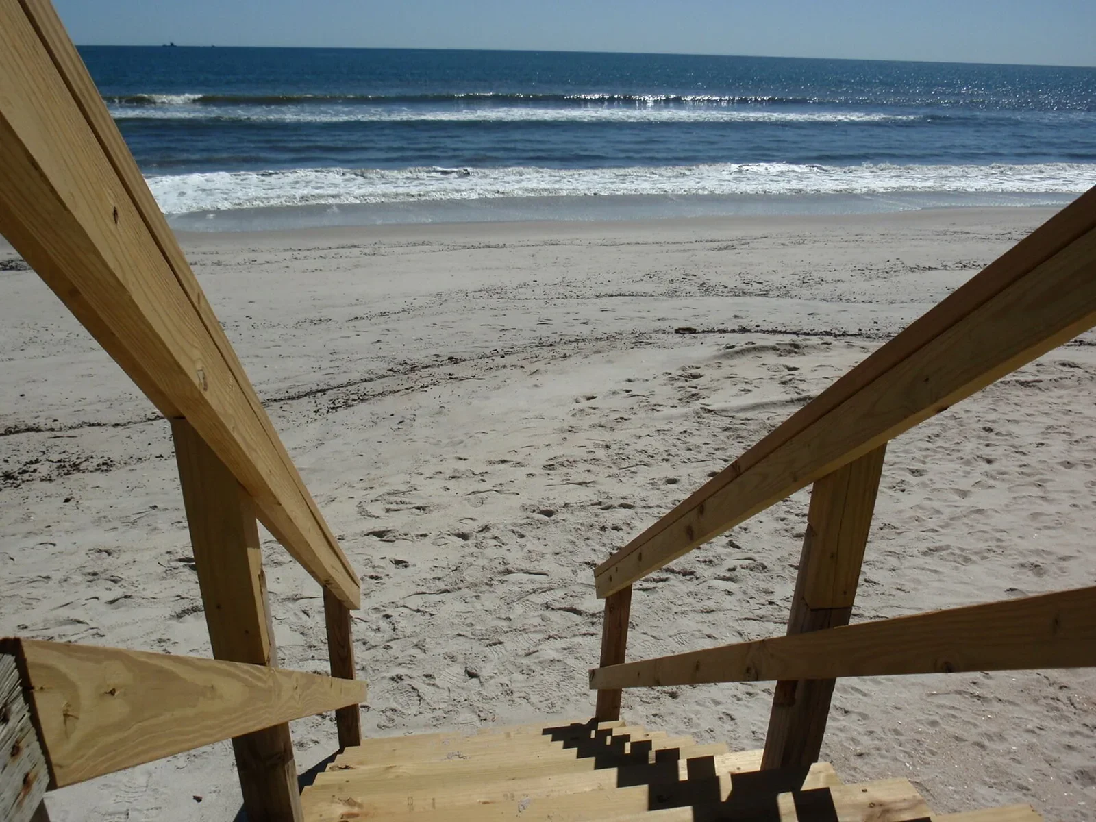 Wooden beach-access stairs descending toward the sand and Atlantic surf