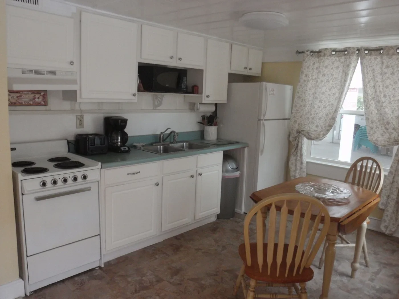 White kitchen cabinets, electric range, refrigerator and small dining table