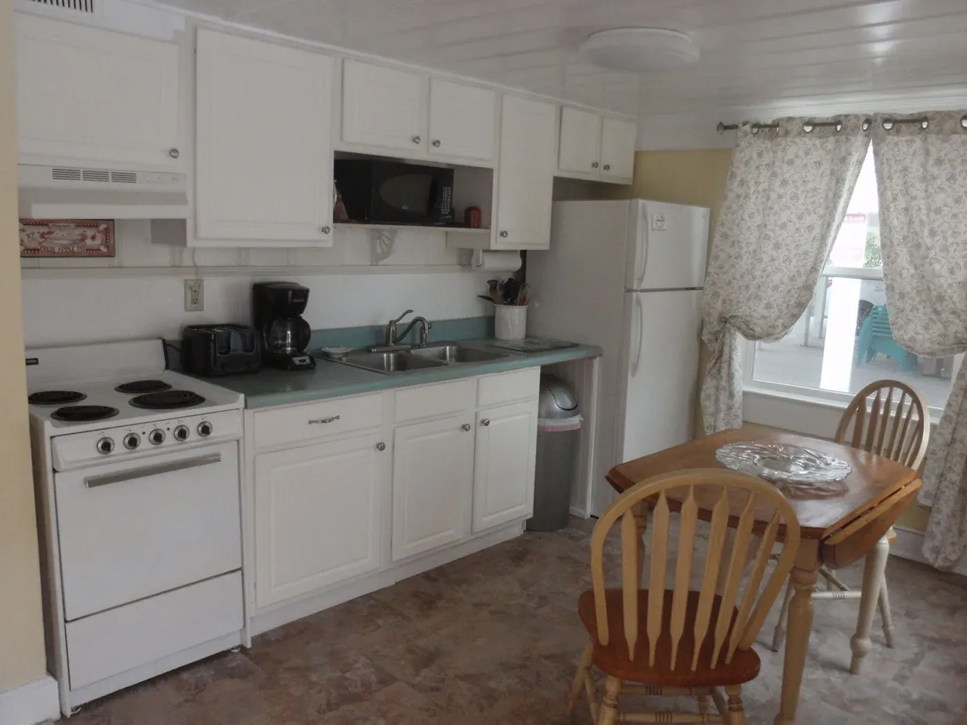 White kitchen cabinets, electric range, refrigerator and a small dining table