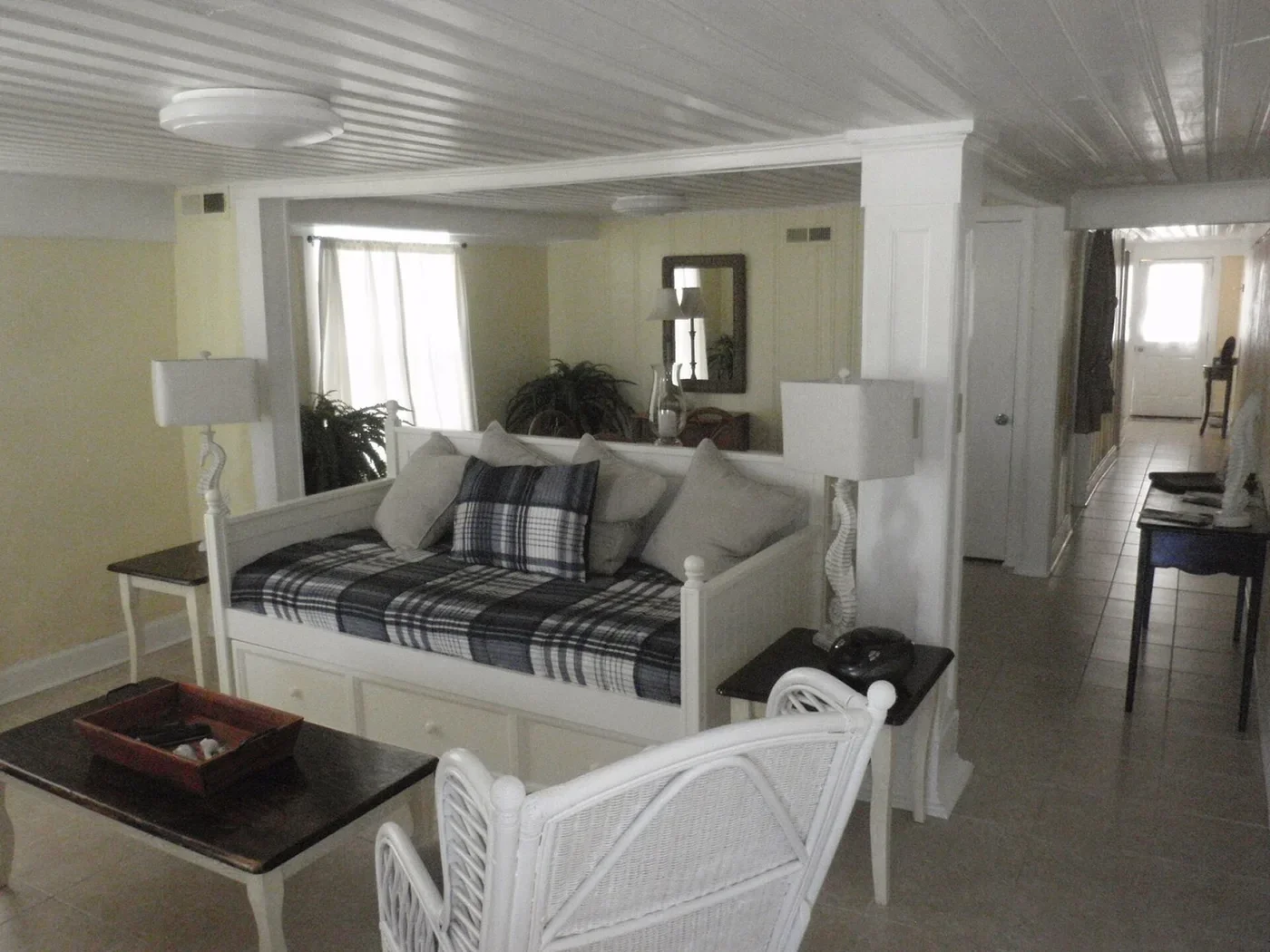 Living area with white daybed-style seating, a wicker chair and an open passage