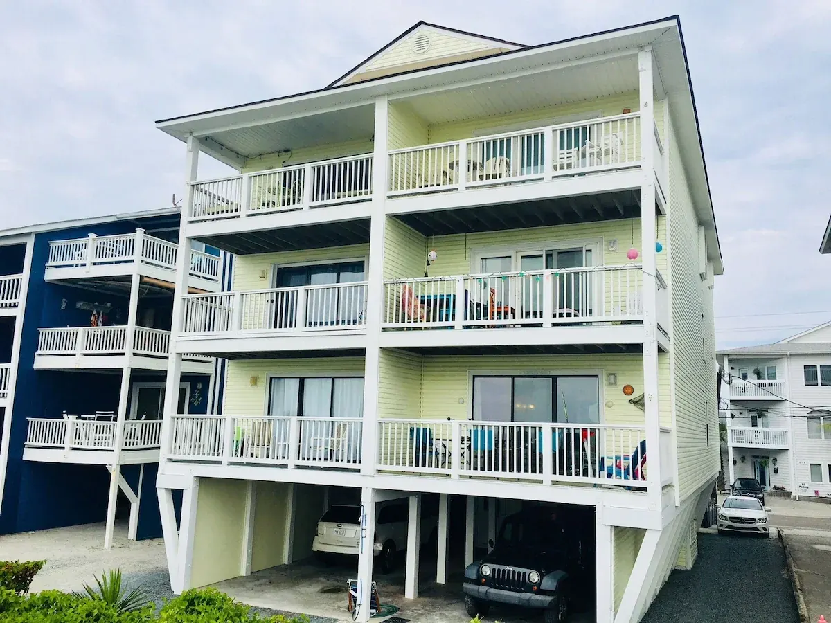 Pale yellow condo building with stacked white-railed balconies and parking beneath
