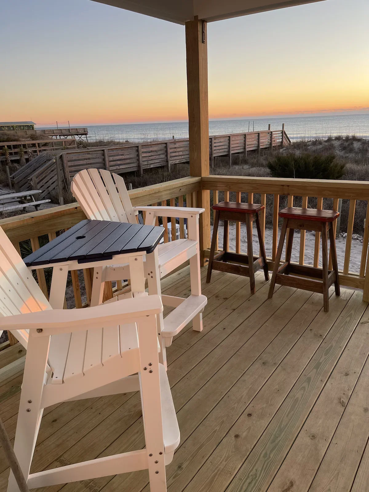 Covered wooden deck with white chairs overlooking the beach and ocean