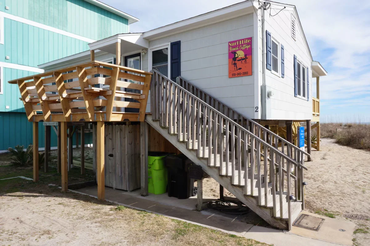 Detached white raised beach cottage with black shutters and wooden exterior stairs