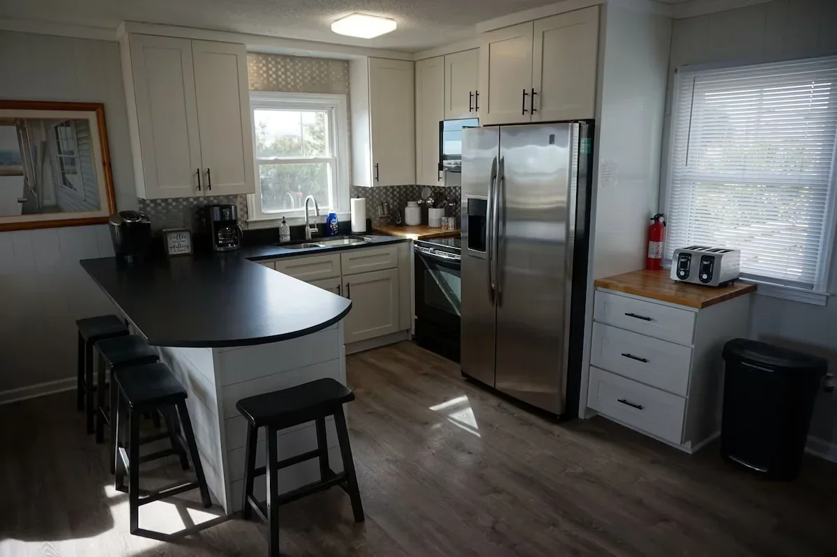 White kitchen cabinets, stainless refrigerator and counter with stools