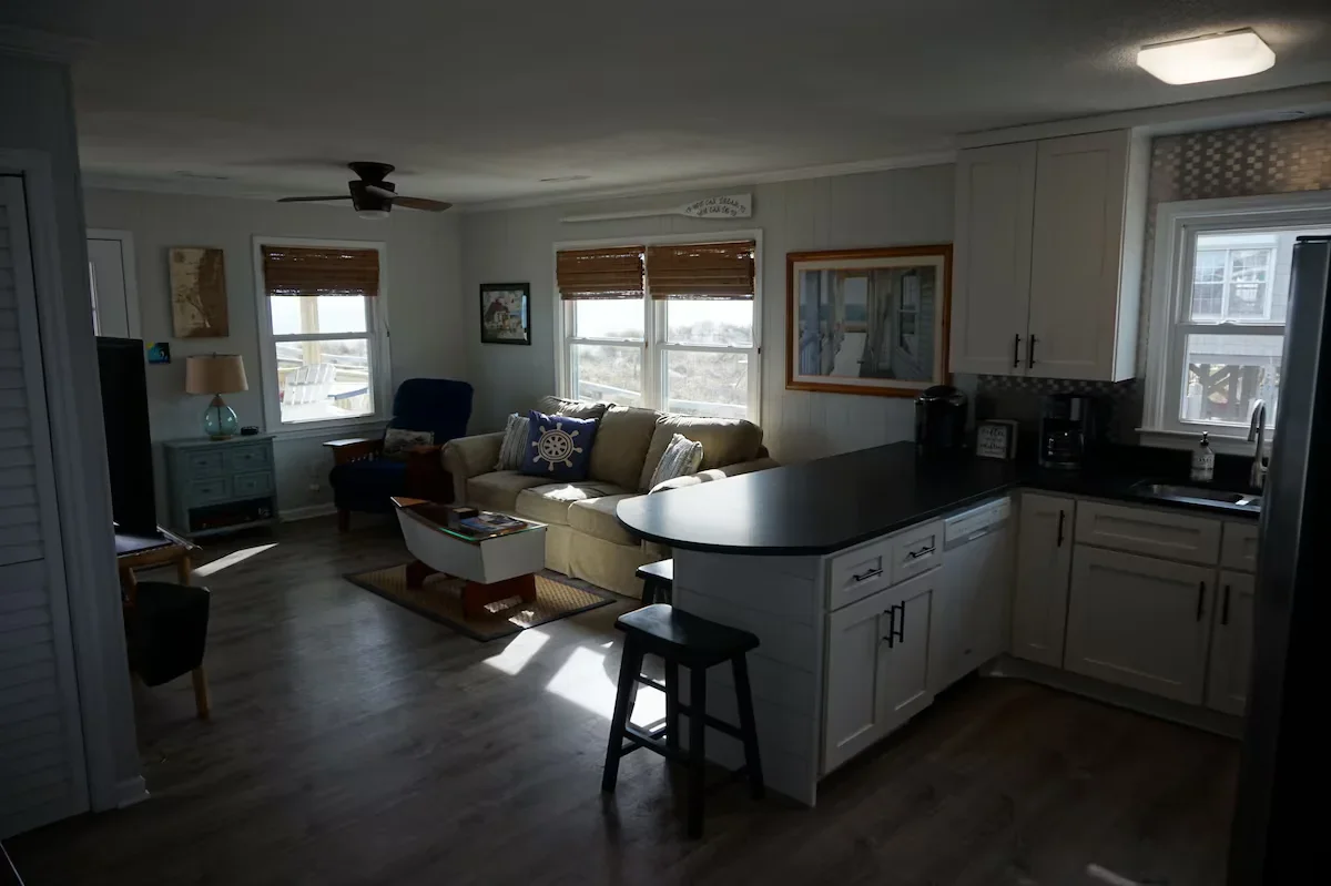 Sofa and armchairs beside ocean-facing windows, with a kitchen counter in the foreground